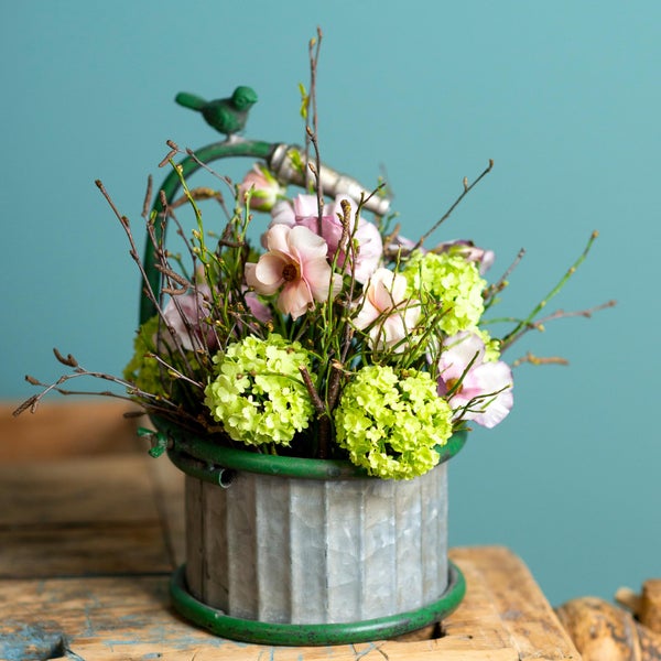 Blumenarrangement mit Hortensien und Magnolien in einem Zinkeimer mit Vogelverzierung als Dekoration.