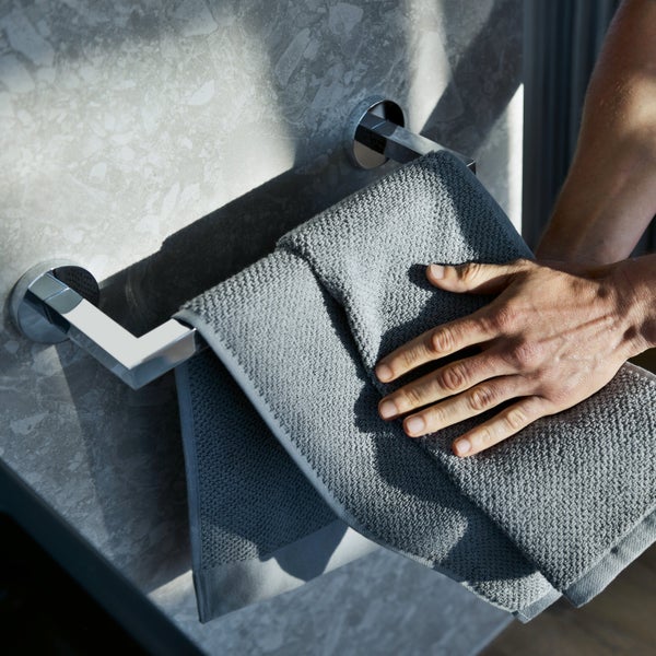 Handtuchhalter aus Metall an einer Steinwand mit einem aufgehängten Handtuch, das mit einer Hand glatt gestrichen wird.