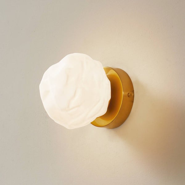 Wandleuchte mit rundem goldfarbenem Sockel und weißem Schirm in organischer Knitteroptik.