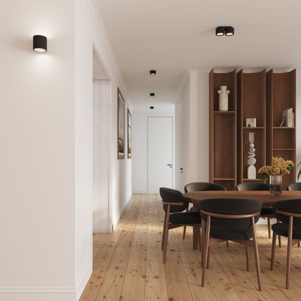 Heller Flur mit Holzboden, schwarzen Wand- und Deckenleuchten, einem hölzernen Esstisch mit Stühlen und einem großen Holzregal.