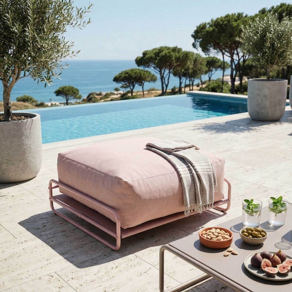 Rosa Outdoor-Puff mit Metallgestell auf einer hellen Terrasse neben einem Pool mit Meerblick.