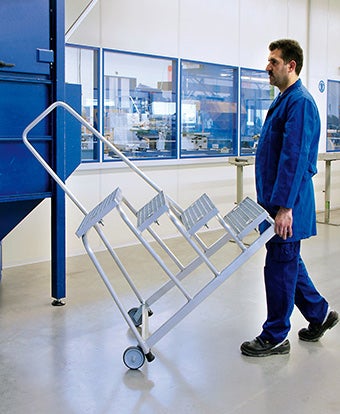 Mann transportiert eine mobile Trittleiter in einer Produktionshalle.