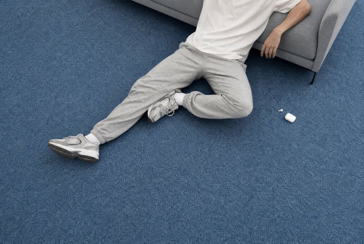 Person sitzt auf strukturiertem blauem Teppichboden im Wohnzimmer neben einem Sofa.