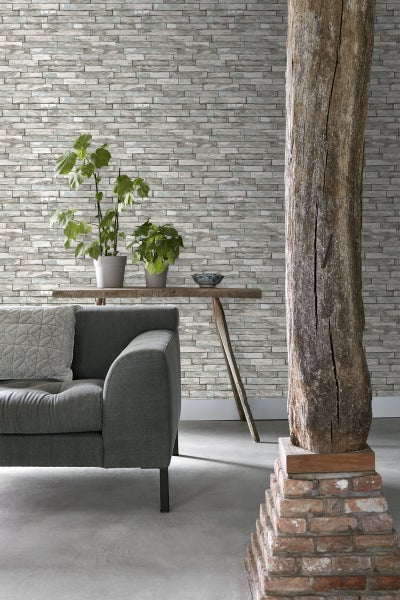 Wohnzimmer mit grauer Steinwandtapete, Sofa, Holztisch, Pflanzen und Holzsäule auf Ziegelsteinsockel.