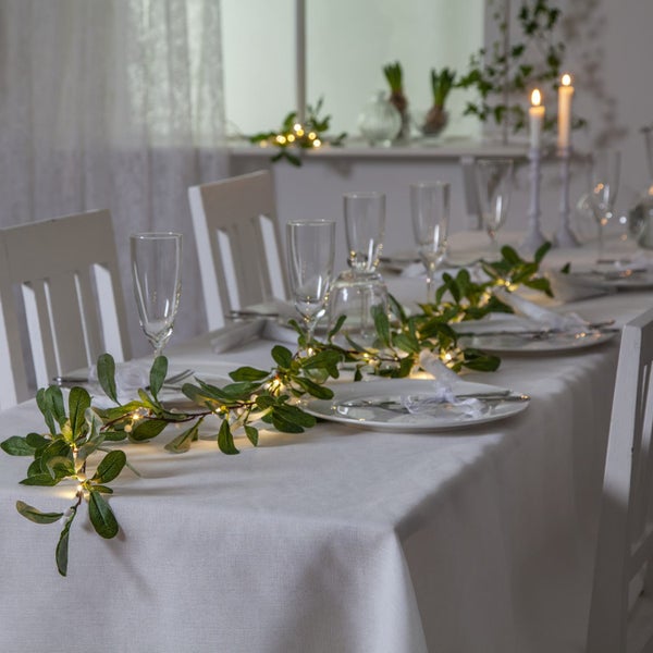 Festlich gedeckter Tisch mit Tischdecke, Geschirr, Gläsern, Stühlen und Lichterkette