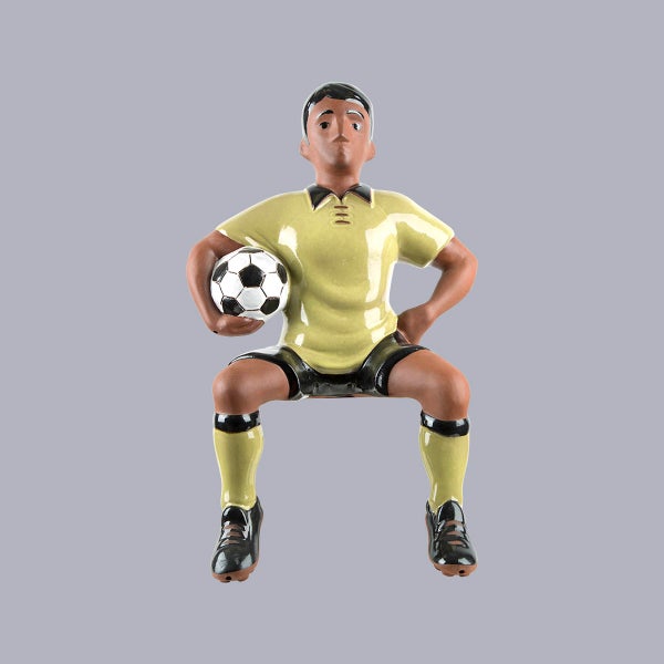 Dekofigur Fußballer sitzend mit Fußball aus glasierter Keramik.