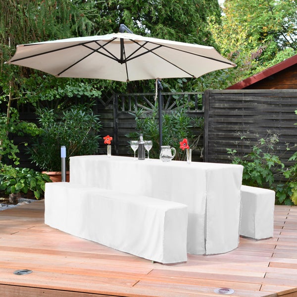 Gartenszene mit Esstisch, Bänken und Sonnenschirm, alle mit weißen Hussen bedeckt