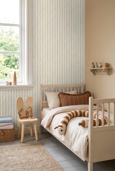 Hell eingerichtetes Kinderzimmer mit einer gestreiften Blumentapete, einem Holzbett, einem Hasenstuhl und hellen Textilien.