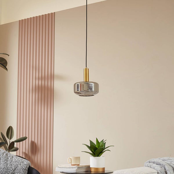 Moderne Pendelleuchte mit rauchgrauem Glasschirm und goldfarbenem Metallelement in einem hellen Wohnzimmer.