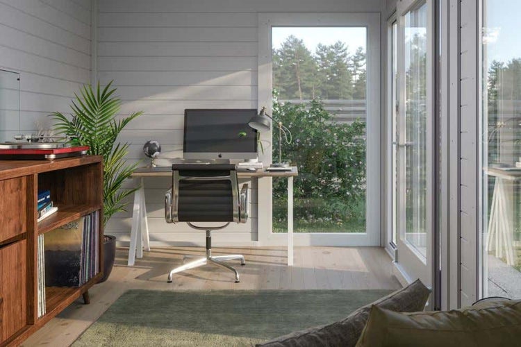 Helles Gartenbüro aus Holz mit Schreibtisch, schwarzem Bürostuhl, Computer-Monitor, großen Glasfenstern und einem Regal aus Holz.