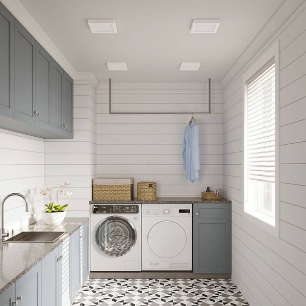 Helle Waschküche mit vier quadratischen LED-Deckenpanels, grauen Schränken, Waschmaschine und Trockner.