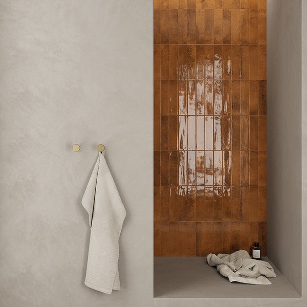 Modernes Badezimmer mit glänzenden Wandfliesen in Rostoptik und glatten, hellen Wänden, ergänzt durch Handtuchhaken und Textilien.