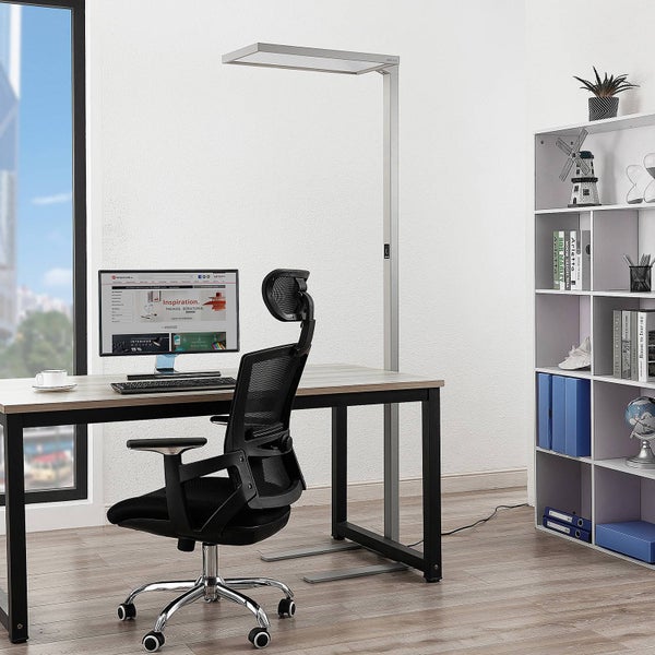 Moderner Arbeitsplatz mit silberner LED-Stehleuchte, Schreibtisch mit Monitor und schwarzem ergonomischem Bürostuhl auf hellem Holzboden.