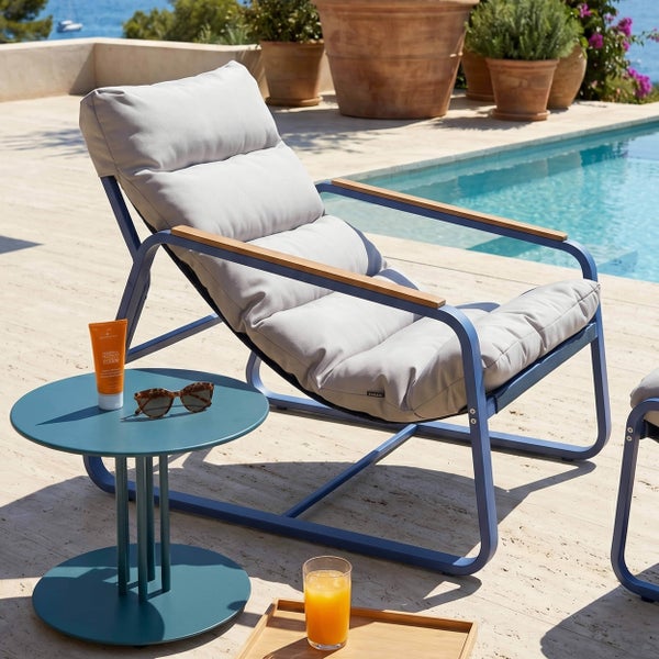 Moderner Garten Loungesessel mit hellgrauer Polsterung, blauem Metallgestell und Holzarmlehnen neben einem runden Beistelltisch am Pool.