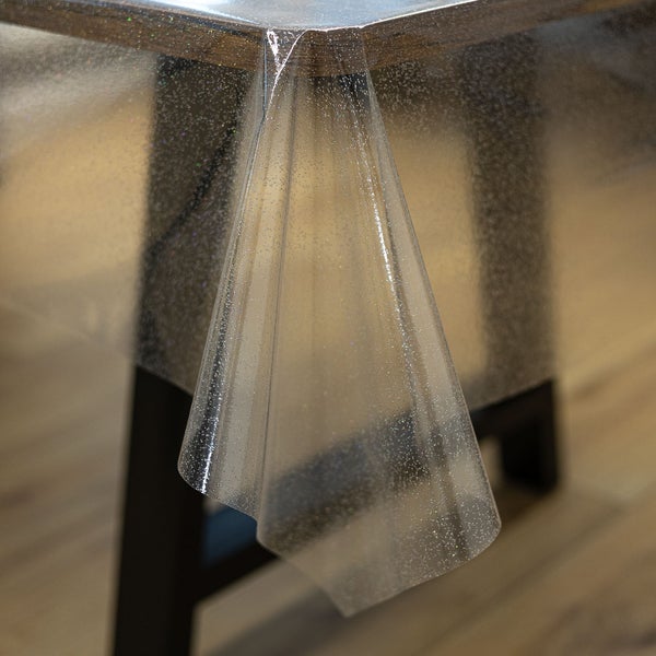 Durchsichtige Tischdecke mit feinen Glitzerpartikeln, über eine Tischecke aus Holz drapiert.