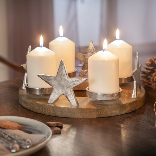 Adventskranz mit vier brennenden Kerzen und Sternmotiven auf einem Holztisch