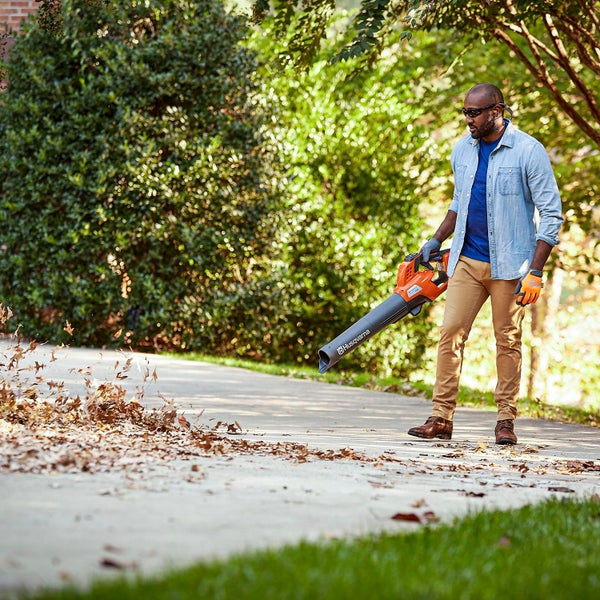Ein Mann benutzt einen Laubbläser von Husqvarna, um Blätter von einem Gehweg zu entfernen.