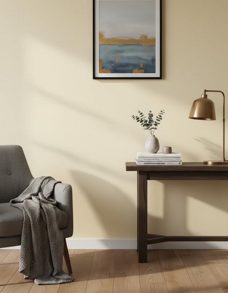 Wohnzimmer mit beiger Wandfarbe, eingerichtet mit einem grauen Sessel, Holztisch, Tischlampe und Wandbild in einer hellen und wohnlichen Umgebung.