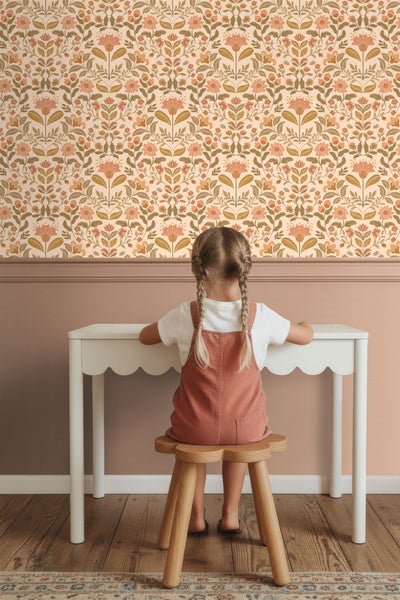 Kind sitzt an einem Tisch vor einer Wand mit Blumentapete.