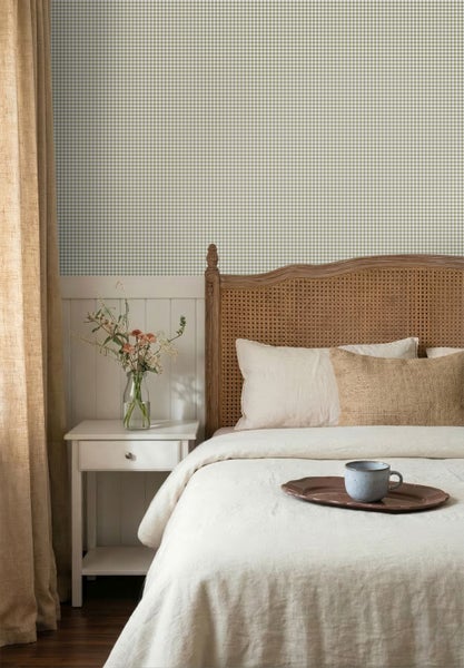 Helles Schlafzimmer mit karierter Tapete, weißen Holzpaneelen, Holzbett mit Geflecht-Kopfteil und neutralem Vorhang im Landhausstil.