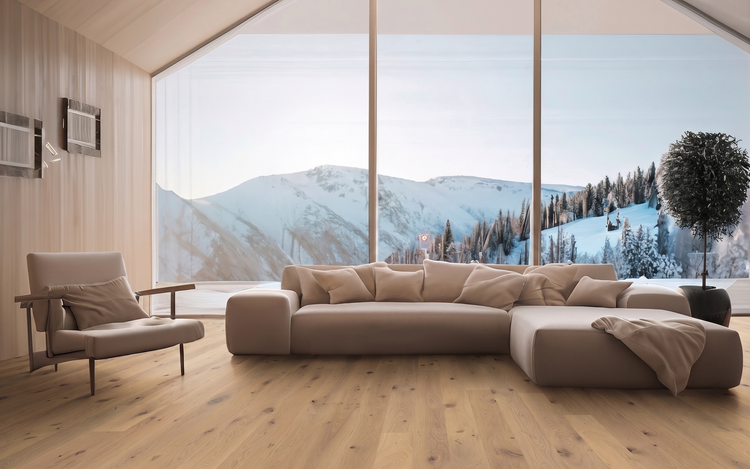 Helles Wohnzimmer mit Eichenparkett, großem beigen Ecksofa, passendem Sessel und Panoramafenster mit Blick auf verschneite Berge.