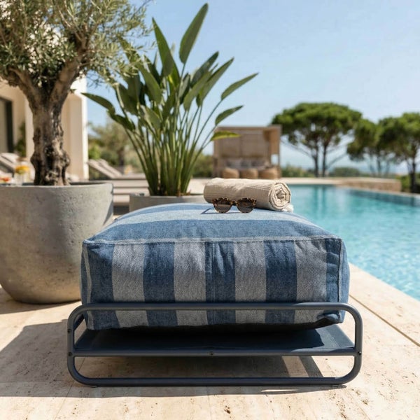 Moderner Outdoor-Pouf mit blau-weiß gestreiftem Kissen auf grauem Metallgestell, am Pool in einem hellen, organisierten Garten platziert.