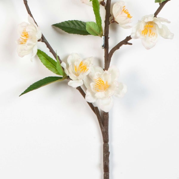 Künstlicher Blütenzweig mit weißen Blüten, gelber Mitte und grünen Blättern auf einem dunklen Stiel.