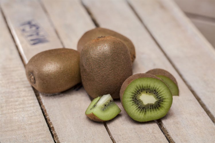 Mehrere ganze Kiwis und eine aufgeschnittene Kiwi liegen auf einer hölzernen Obstkiste.