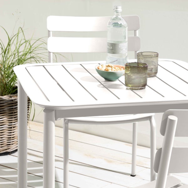 Weißes Gartenmöbel-Set aus Metall mit rechteckigem Tisch in Lattenoptik und passenden Stühlen auf einer hellen Terrasse.