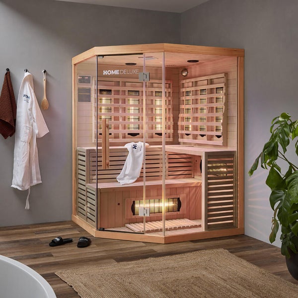 Ecksauna aus Holz mit Infrarotstrahlern und Glastür im modernen Badezimmer mit Bademantel und Pflanze.