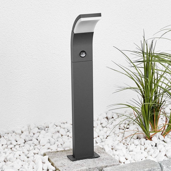 Moderne anthrazitfarbene LED-Wegeleuchte mit Bewegungsmelder, platziert auf weißen Steinen neben einer Gartenpflanze.