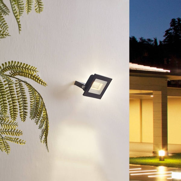 Schwarzer quadratischer LED-Außenstrahler an einer Hauswand montiert, warmes Licht in einer abendlichen Szenerie.