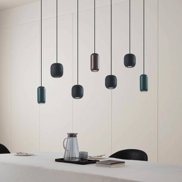 Moderne Pendelleuchten in verschiedenen Formen über einem minimalistisch gedeckten Esstisch vor einer hellen Wand.
