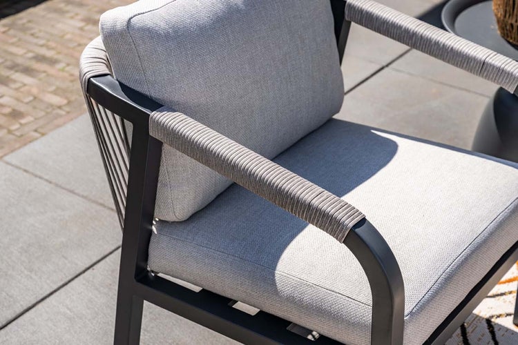 Gartenstuhl mit schwarzem Metallrahmen, grauer Seilwicklung an den Armlehnen und hellgrauen Polstern auf einer Terrasse.