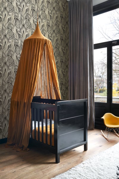 Ein Kinderzimmer mit einem schwarzen Gitterbett und einem Baldachin