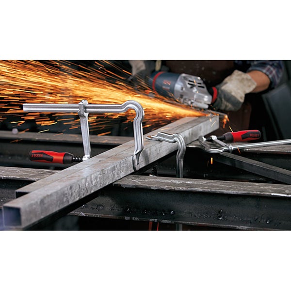 Zwei Werkstückspanner halten ein Metallstück, während ein Winkelschleifer Funken sprüht.