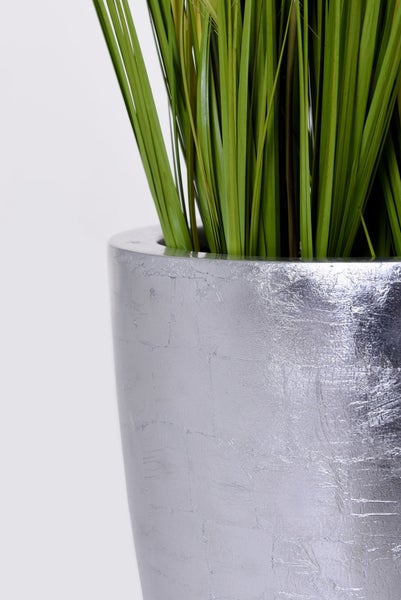 Detailaufnahme eines silbernen Pflanzgefäßes mit künstlichem Gras.
