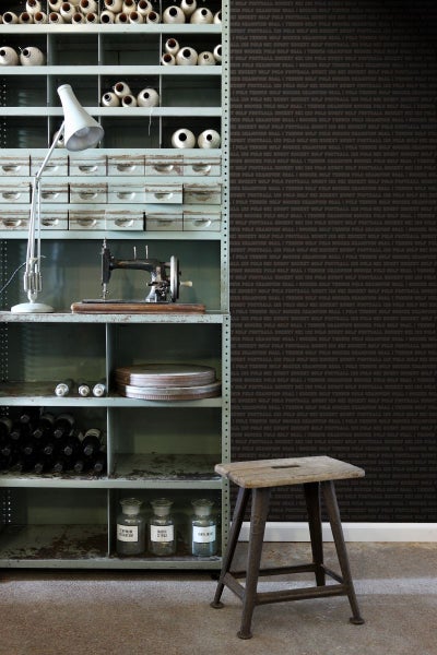 Regal mit Nähmaschine, Lampe, Garnrollen, Flaschen und Gläsern sowie Hocker vor einer dunklen Wand mit Textmuster