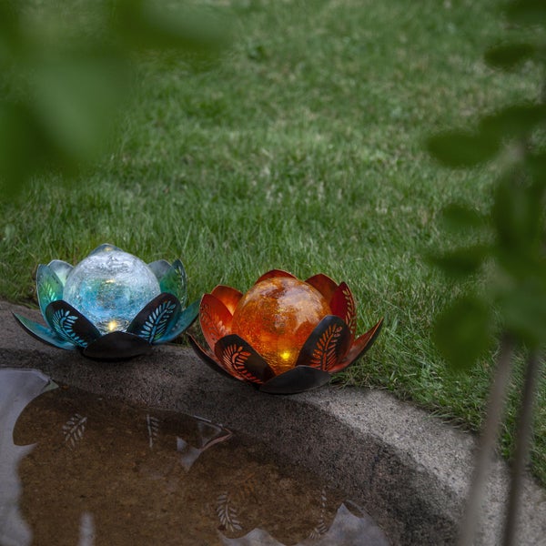 Zwei Gartenleuchten mit Glaskugeln und Metallelementen in Blumenform auf Stein