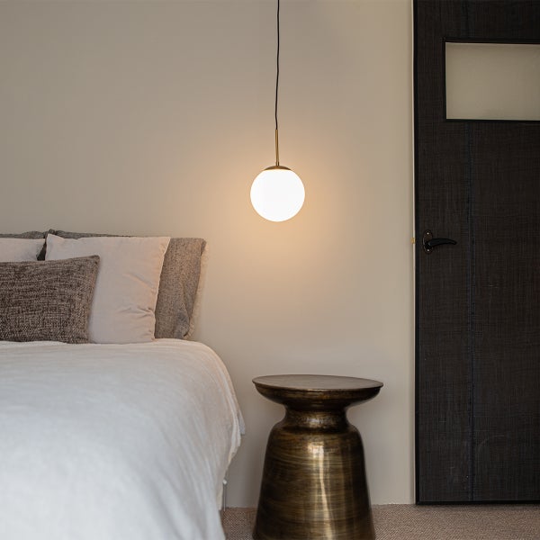 Schlafzimmer mit Bett, Nachttisch und Hängelampe mit Kugelschirm.