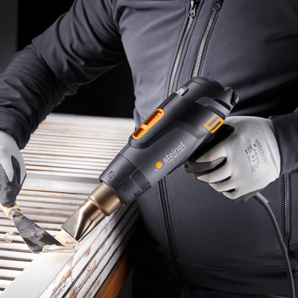 Heißluftpistole Steinel PRO HG 2320 E beim Entfernen von Farbe von Holzleisten mit einem Spachtel.