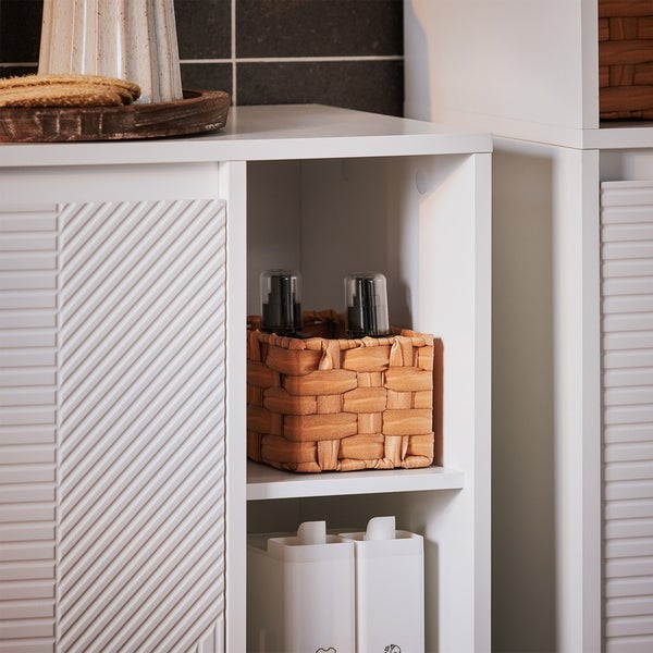 Detailaufnahme eines weißen Badezimmerschranks mit Stauraum und geflochtenem Korb