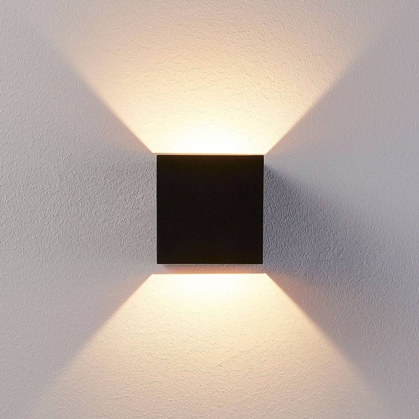 Quadratische Wandleuchte in Schwarz mit Lichtkegeln nach oben und unten an einer strukturierten Wand.