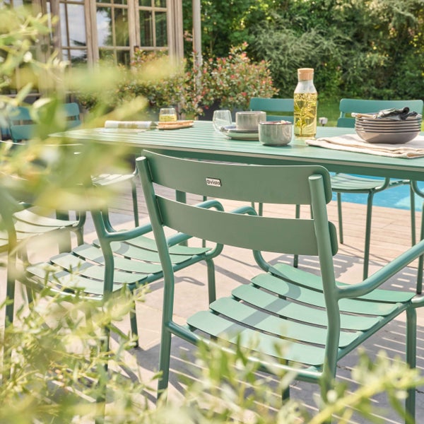 Modernes Gartenmöbel-Set aus grünem Metall mit Tisch und Stühlen auf einer Terrasse am Pool. Oviala Logo.