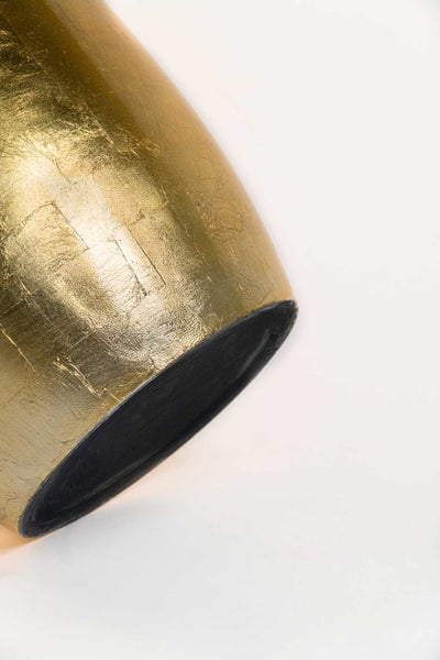Detailaufnahme eines zylindrischen Dekorationsobjekts mit strukturierter Oberfläche in Goldblattoptik und schwarzer Innenseite.
