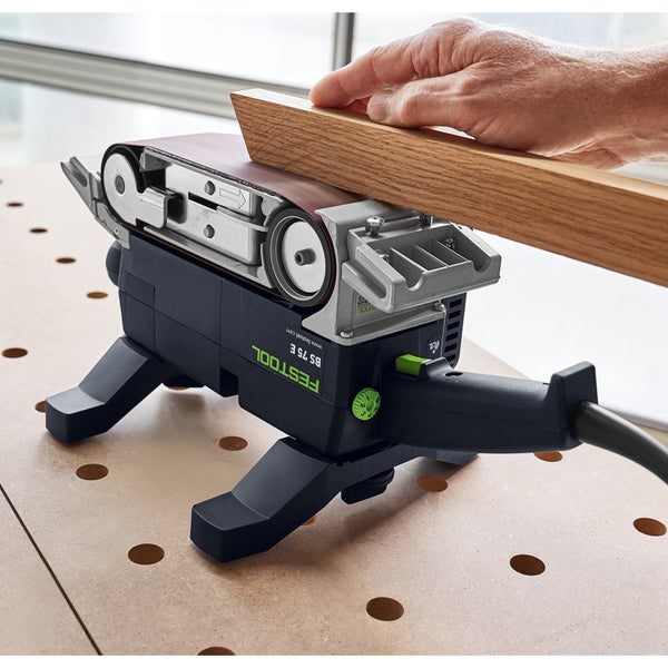 Festool Bandschleifer BS 75 E stationär zum Schleifen einer Holzleiste auf einem Arbeitstisch.