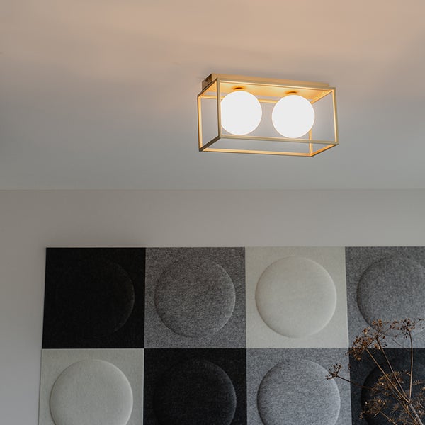 Moderne Deckenleuchte mit zwei weißen Glaskugeln in einem rechteckigen, goldfarbenen Metallrahmen in einem hellen, modern eingerichteten Raum.