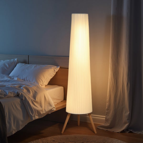 Moderne Stehleuchte mit plissiertem Schirm und hölzernem Dreibein-Stativ in einem Schlafzimmer.