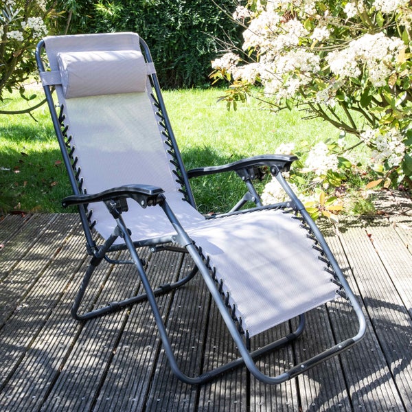Moderner Relaxsessel mit Kopfstütze und Armlehnen auf einer sonnigen Holzterrasse in einem Garten mit blühenden Sträuchern.