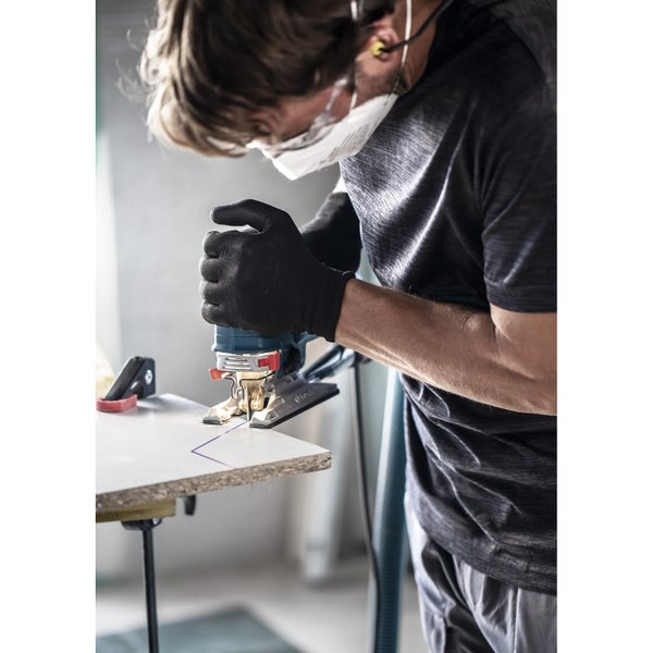 Mann mit Schutzmaske und Handschuhen sägt Holzplatte mit einer Stichsäge
